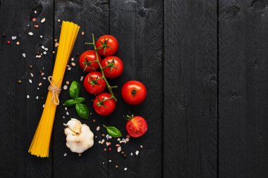 Gıda arka plan lezzetli İtalyan yemekleri için ile spagetti, domates, sarımsak, fesleğen ve Himalaya tuz. Çeşitli pişirme malzemelerin üzerine siyah ahşap masa. Menü veya yemek tarifleri için kopya alanı ile üstten görünüm.