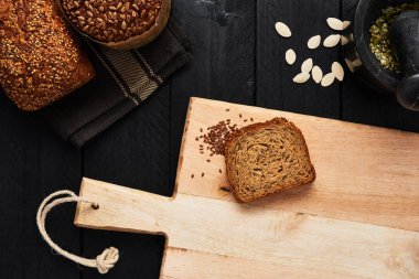 Dilim ekmek, keten tohumu ve çeşitli huysuz kepekli ekmek, kabak çekirdeği ve harç siyah ahşap masa üzerinde kesme tahtası. Üstten görünüm.
