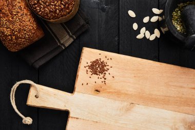 Doğrama Kurulu keten tohumu ve çeşitli huysuz kepekli ekmek, kabak çekirdeği ve harç siyah ahşap masa üzerinde. Kopya alanı metin, menü veya yemek tarifleri ile üstten görünüm.