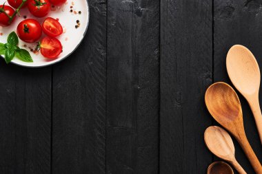 Çeşitli tahta kaşıklar ve domates ile Himalaya tuz, biber ve fesleğen siyah ahşap masa üzerinde bir tabak içinde. Üstten Görünüm menüsü veya yemek tarifleri için kopya alan ile. Gıda arka plan kavramı.