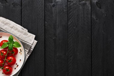 Siyah ahşap masa üzerinde gri dishtowel üzerinde üstten görünüm domates Himalaya tuz, biber ve fesleğen ile bir tabak içinde. Üstten Görünüm menüsü veya yemek tarifleri için kopya alan ile. Gıda arka plan kavramı.