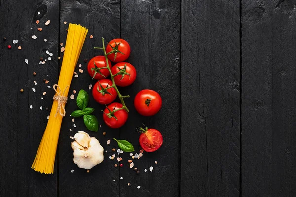Gıda arka plan lezzetli İtalyan yemekleri için ile spagetti, domates, sarımsak, fesleğen ve Himalaya tuz. Çeşitli pişirme malzemelerin üzerine siyah ahşap masa. Menü veya yemek tarifleri için kopya alanı ile üstten görünüm.