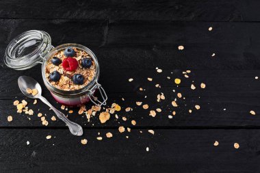 Üstten görünüm sağlıklı kahvaltı. Frambuaz sos, yulaf ve kopya alanı ile siyah ahşap masa üzerinde yaban mersini ile sağlıklı yoğurt kavanoz.