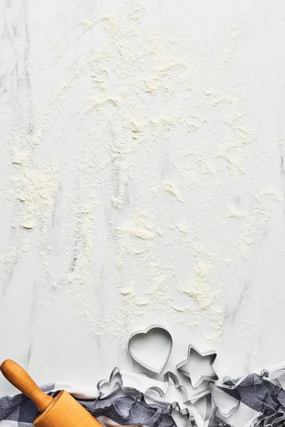 Baking background for baking Christmas cookies with cutters and rolling pin on white marble table with flour. Top view, copy space for text.