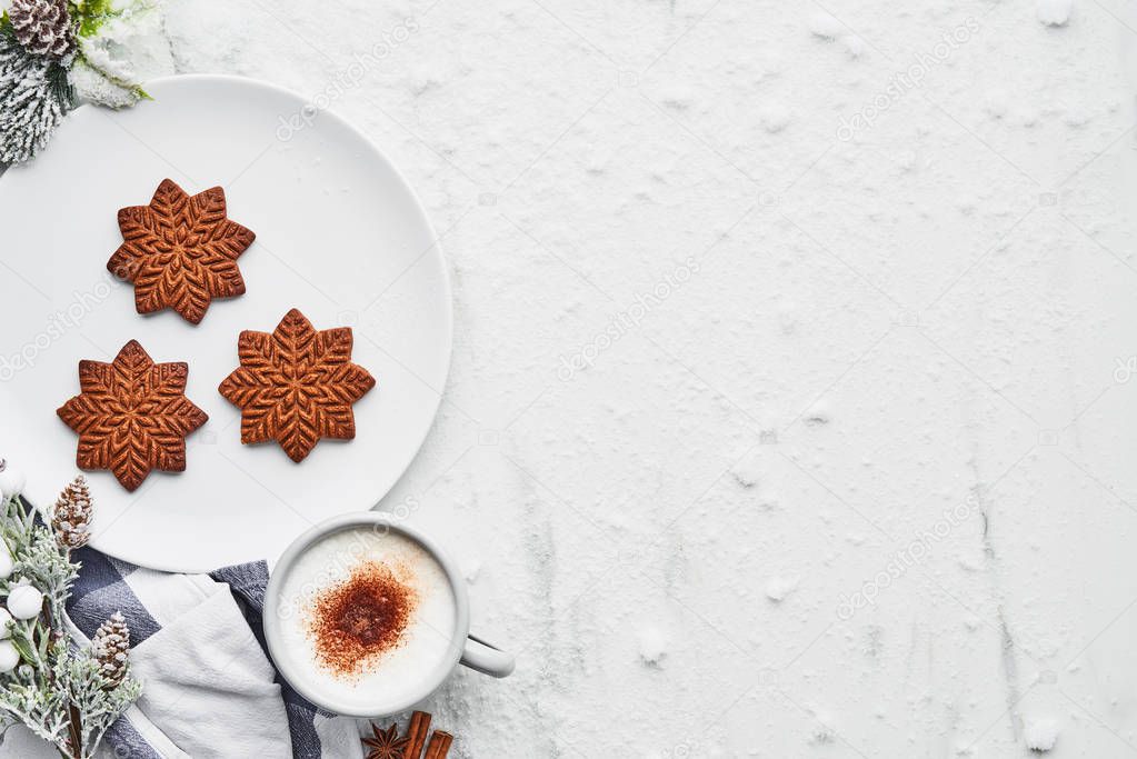 Gingerbread cookies with hot cocoa drink or eggnog on white marble table covered with snow. Top view of snowflake shape gingerbread cookies with copy space.