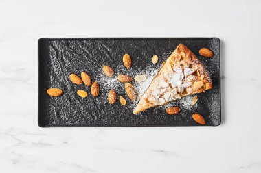 Şeker ve badem siyah plaka üzerinde beyaz mermer masa üzerinde buzlanma ile elma ve badem pasta dilimlenmiş. Üstten görünüm.