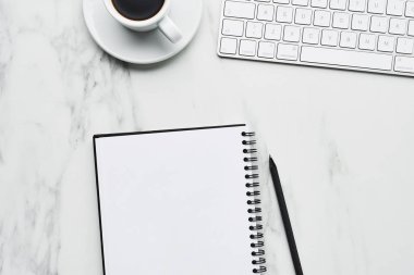 Beyaz bilgisayar klavye, kahve fincanı ve defter kalem üzerinde beyaz mermer zemin ile iş kompozisyon. Office kavramı, kahve molası. Kopya alanı ile üstten görünüm