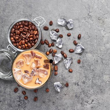 Soğuk buzlu kahve cam ve cam gri beton zemin üzerine kahve çekirdekleri demlenmiş. Çikolata, vanilya, karamel veya tarçın buzlu kahve uzun bardak. Üstten görünüm, kare kırpma.