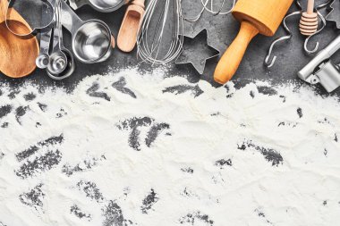 Mutfak gereçleri ve un pişirme veya arka plan yemek için. Haddeleme pin, çırpma teli, tahta kaşık, çerez kesici ve metin için kopya alanı koyu gri beton zemin üzerine kaşık ölçme. Üstten görünüm.