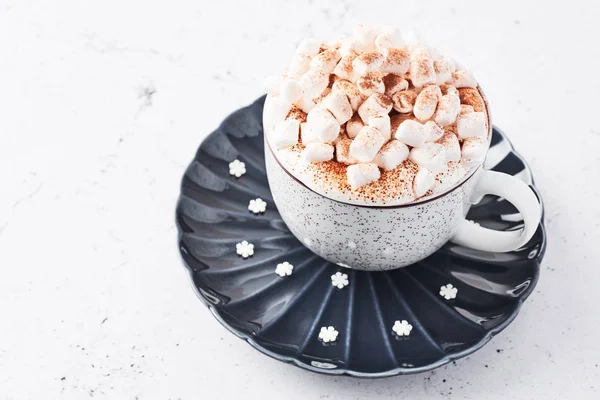 Hot chocolate or cocoa with whipped cream and marshmallow candy sprinkled with cinnamon or cocoa powder over white marble table with copy space for text. Selective focus.