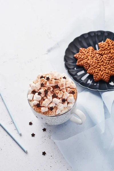 Hot chocolate or cocoa with whipped cream and marshmallow candy sprinkled with cinnamon or cocoa powder with chocolate stars and Christmas gingerbread cookies on blue serving plate. Copy space.