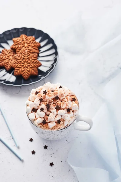 Hot chocolate or cocoa with whipped cream and marshmallow candy sprinkled with cinnamon or cocoa powder with chocolate stars and Christmas gingerbread cookies on blue serving plate. Top view.