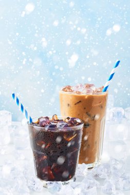 Kış içecek bir bardak kahve ve buzlu kahve krem buz beyaz mermer masa üstünde kar ile mavi arka plan üzerinde çevrili uzun bir bardak buzlu. Seçici odak, kopya alanı metin için.
