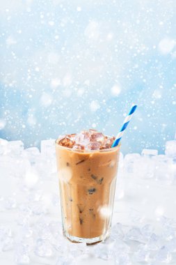 Kış kar ile mavi arka plan üzerinde beyaz mermer masa buza çevrili saman ile uzun bir bardak krem buz kahve iç. Seçici odak, kopya alanı metin için.