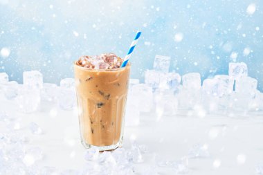 Kış kar ile mavi arka plan üzerinde beyaz mermer masa buza çevrili saman ile uzun bir bardak krem buz kahve iç. Seçici odak, kopya alanı metin için. Yatay.