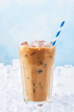 Yaz ile mavi arka plan üzerinde beyaz mermer masa buza çevrili saman ile uzun bir bardak krem buz kahve iç. Seçici odak, kopya alanı metin için.