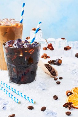 Kış içecek bir bardak kahve ve buzlu kahve krem buz, kahve çekirdekleri ve beyaz mermer tablosundaki çeşitli baharatlar kar ile mavi arka plan üzerinde çevrili uzun bir bardak buzlu. Kopya alanı.