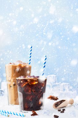 Kış içecek buzlu cam ve buz kahve kahve krem buz küpleri, kahve çekirdekleri ve çeşitli baharatlar kar üzerinde mavi arka plan üzerinde çevrili uzun bir bardak. Metin için yer kopyalayın.