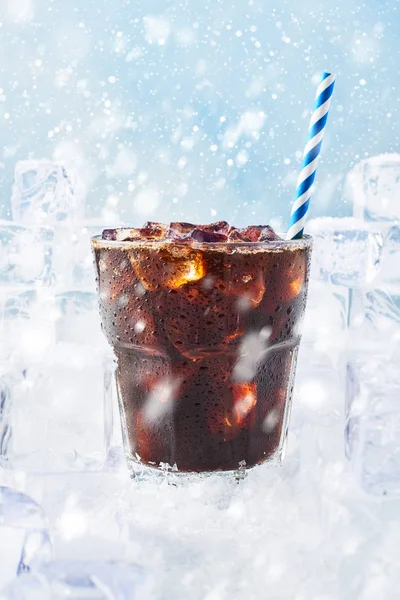 Kış içecek buzlu kahve bir bardak buz üstünde kar kar ile mavi arka plan üzerinde çevrili saman ile. Seçici odak, kopya alanı metin için.