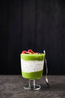 Cam yeşil sağlıklı güler yüzlü. Siyah ahşap arka plan üzerinde yaban mersini, ahududu ve badem karanlık beton masada tepesinde kivi, muz, ıspanak, elma ve chia tohum güler yüzlü. Kopya alanı.