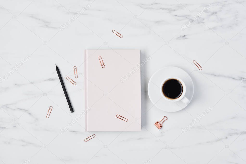 Office desk with coffee cup, paper clips, pencil and pink diary on white marble background. Flat lay. Copy space for text. Top view.