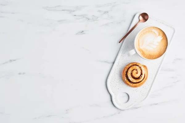 Fırından yeni çıkmış baharat ve kakao doldurma ve kahve ile tarçın rulo veya cappuccino latte art plaka beyaz mermer arka plan üzerinde hizmet veren beyaz tarih ile. Üstten Görünüm. Metin için yer kopyalayın. İsveçli Kahvaltı.