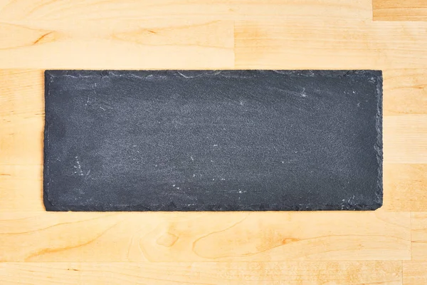 Placa negra de pizarra o piedra negra sobre fondo de madera . — Foto de Stock