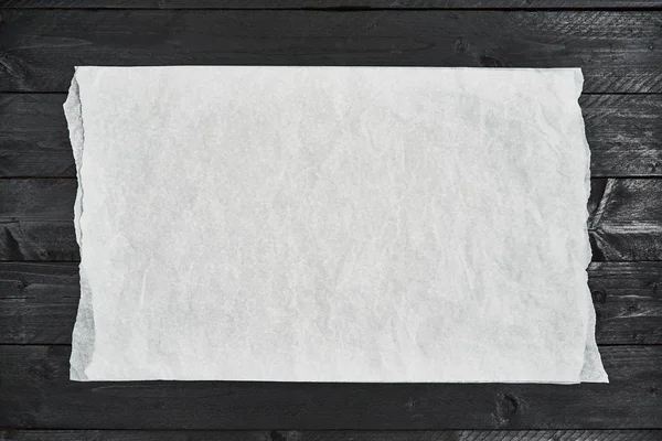 Trozo arrugado de pergamino blanco o papel para hornear en madera negra — Foto de Stock