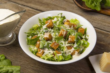 Sezar salatası eski bir ahşap masada beyaz bir kasede soslu ve parmesanlı yapraklarla. Seçili odak.