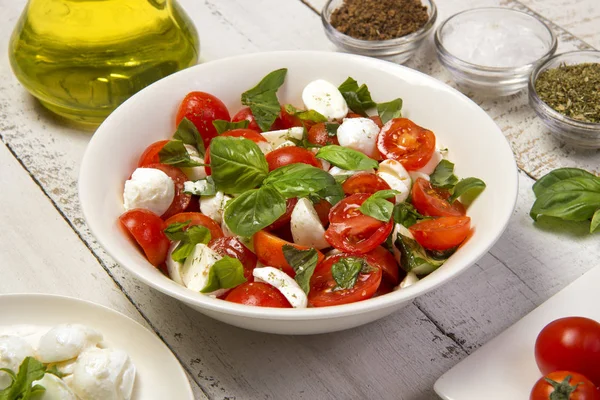 Beyaz ahşap bir masada yuvarlak, beyaz bir salata kasesinde geleneksel Caprese salatası. Seçili odak.