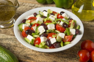 Eski ahşap bir masada yuvarlak beyaz bir kasede Yunan salatası. Seçili odak