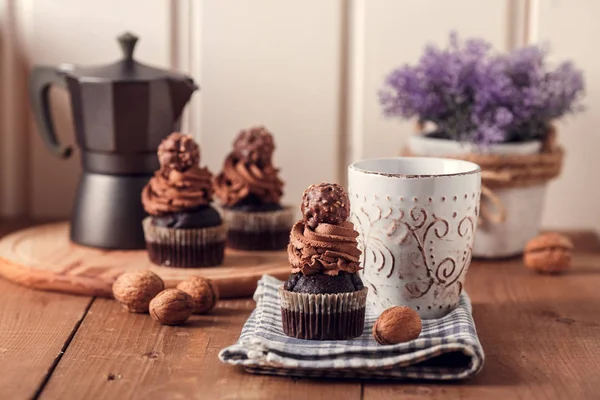 Tasty chocolate cupcakes on wooden board. Cup of coffee. Geyser coffee maker. Violet flowers