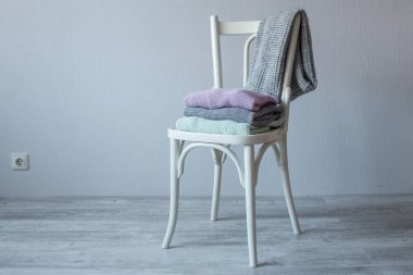 Bir tahta sandalyede rahat örme elbise yığını. Gri duvar