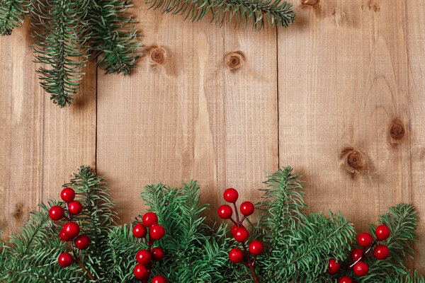 Christmas fir tree on wooden background. Red berries. Rustic style. Top view. Copy space.