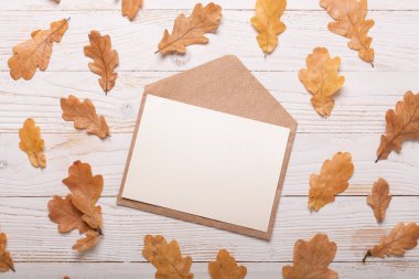 Beyaz ahşap arka planda sonbahar yaprakları ve zarf. Düz konum, üst görünüm, kopyalama alanı.