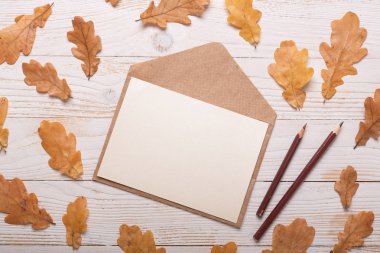 Beyaz ahşap arka planda sonbahar yaprakları ve zarf. Düz konum, üst görünüm, kopyalama alanı.