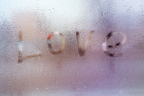 The word Love , rain or water drops on window glasses. Abstract background.