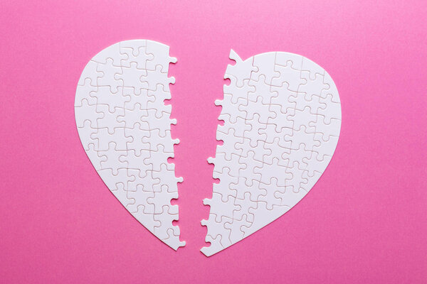 White puzzle broken heart on pink background. Missing piece. Top view