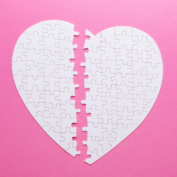 White puzzle broken heart on pink background. Missing piece. Top view