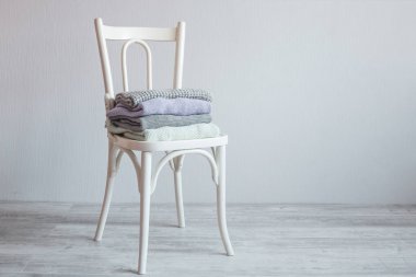 Bir tahta sandalyede rahat örme elbise yığını. Gri duvar. Vintage renklendirme