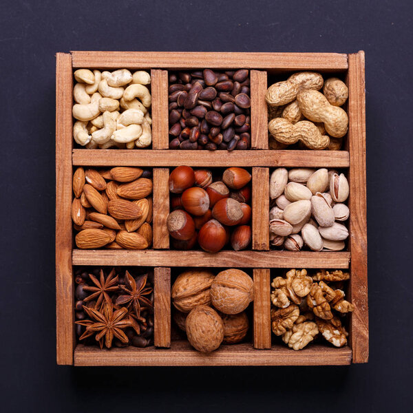 Assortment of nuts in a wooden box on a black background - healthy snack. Top view. Copy space