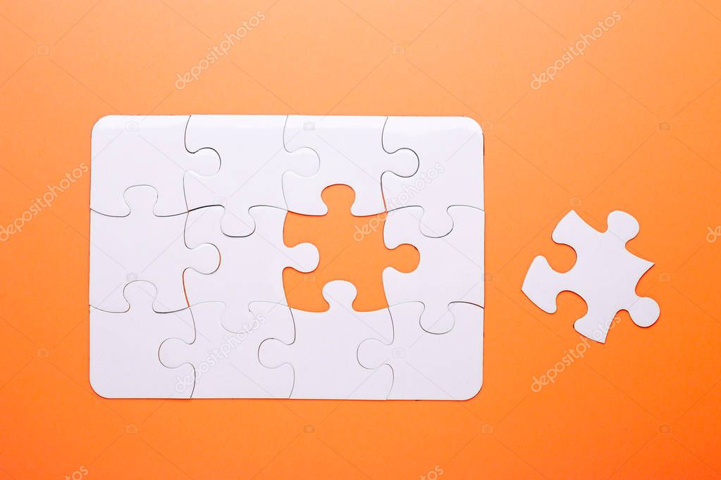White puzzle on orange background. Missing piece. Top view