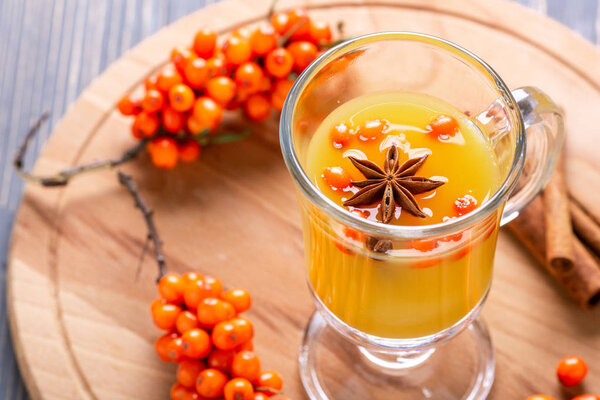 Hot beverage of sea-buckthorn berries in glass cup on wooden background. Rustic style.