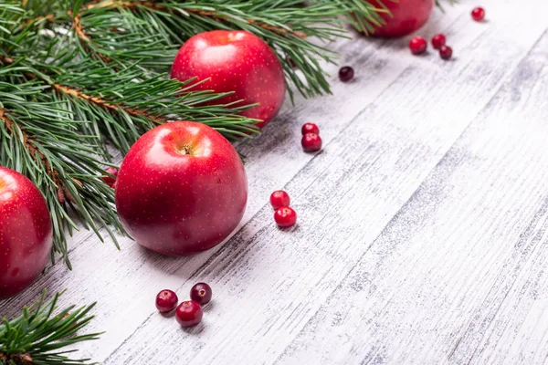 Karácsonyi háttér faágakat, piros alma és áfonya. Világos fából készült asztal — Stock Fotó