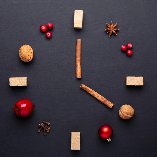 A clock in the form of spice for mulled wine. Cinnamon, anise stars, cranberries, brown sugar. Concept, creative work. Time to cook mulled wine. Top view. Black background