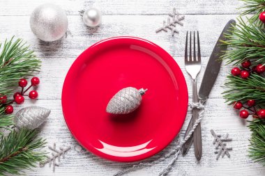 Kırmızı tabak ve gümüş çatal bıçaklı Noel sofrası. Ağaç dalları, kutsal meyveler. Kopyalama alanı olan üst görünüm.