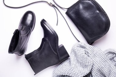 Kadın aksesuar. Beyaz arka planda siyah şık çizmeler, siyah lüks deri çanta, gri eşarp. Üstten görünüm arka plan. Düz yatıyordu. Kopya alanı.