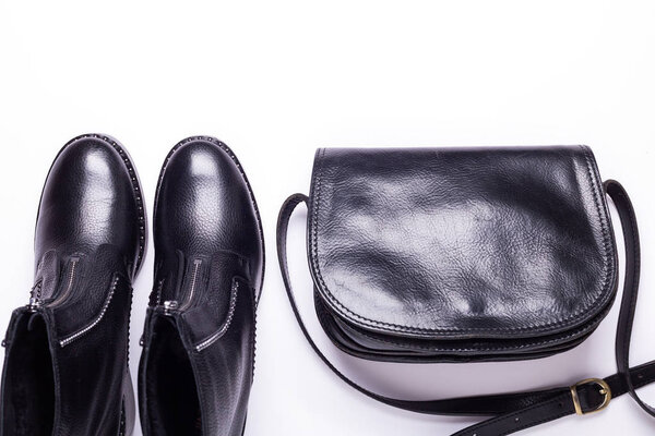 Женский аксессуар. Черные стильные сапоги, черная роскошная кожаная сумка на белом фоне. Вид сверху. Плоский лежал. Копирование пространства
.