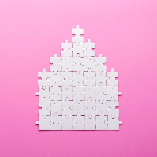 White puzzle. House shape puzzle. The concept of rent, mortgage. Pink background. Top view. Copy space