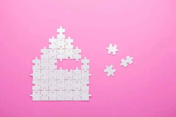 White puzzle. House shape puzzle. The concept of rent, mortgage. Pink background. Top view. Copy space
